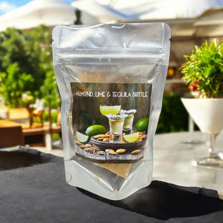 Bag of Almond Lime Tequila Brittle on outdoor patio with umbrellas, shrubs and cocktail